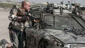 Matt Damon takes cover behind a military vehicle (and his metal exoskeleton) in Elysium.