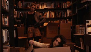 Gaby Hoffmann (standing) tries to cheer up a disconsolate Jenny Slate (in box) in Obvious Child.