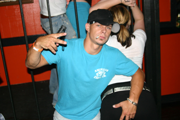 A Club Patron hip-hopper displays some of the genre’s trademarks: hand signs, dangling ciggy, cocked hat, and sexist attitudes toward women.
