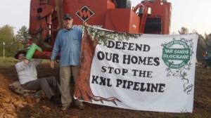 Sam Avery (left) is locked to a tree-cutter at the tar sands blockade, while Gary Stuard holds a protest banner. Coutesy Tar Sands Blockade