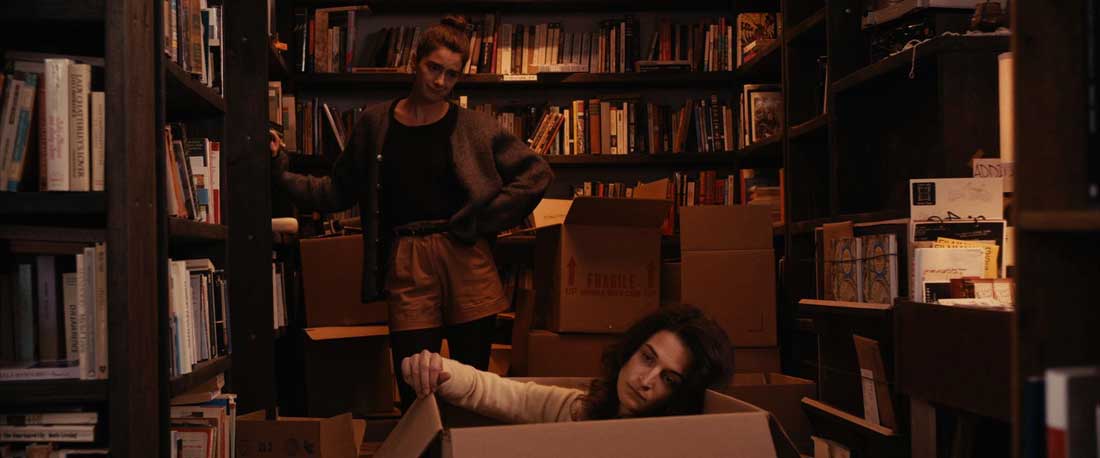 Gaby Hoffmann (standing) tries to cheer up a disconsolate Jenny Slate (in box) in Obvious Child.