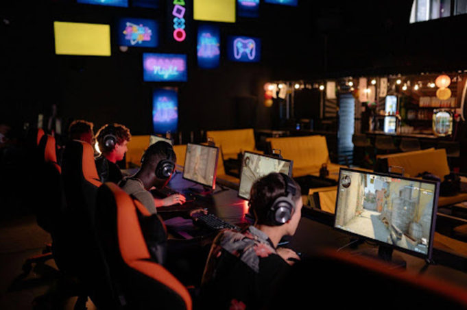Group of gamers wearing headsets playing multiplayer PC games in a neon-lit esports arena.